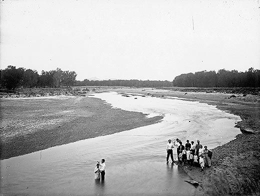 Man baptizing woman in a river with people watching