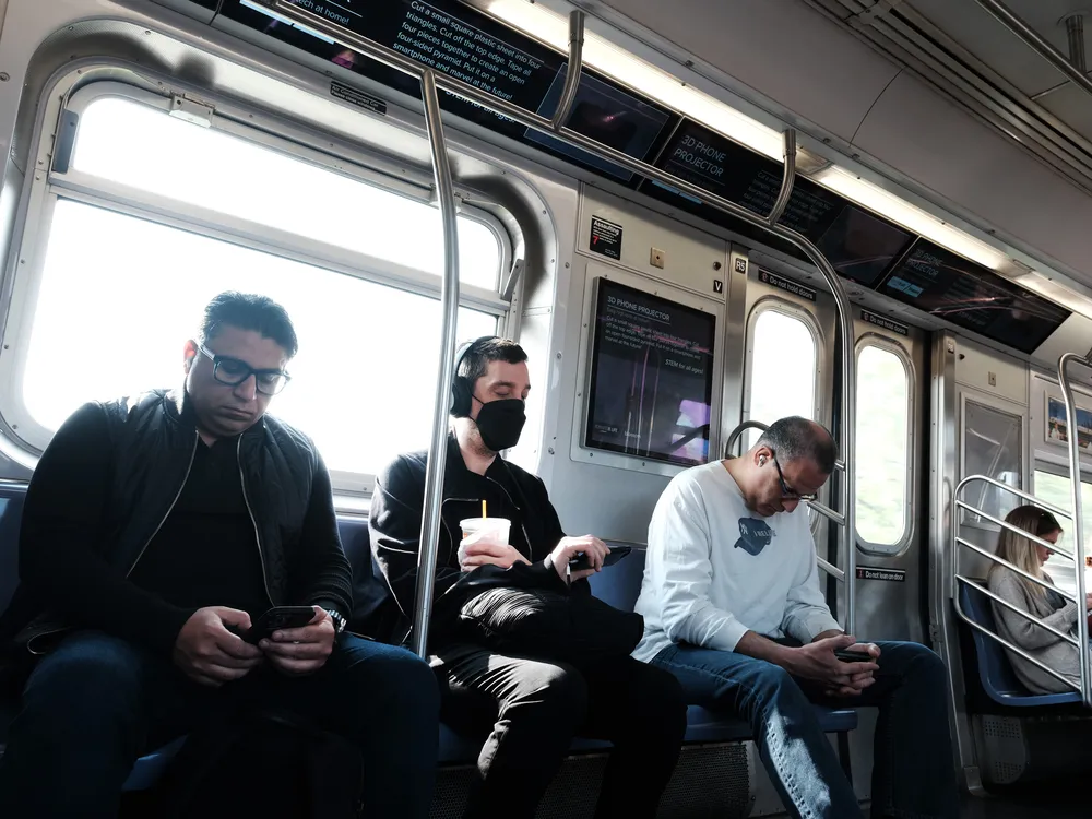 People sitting on a train, one with a mask on