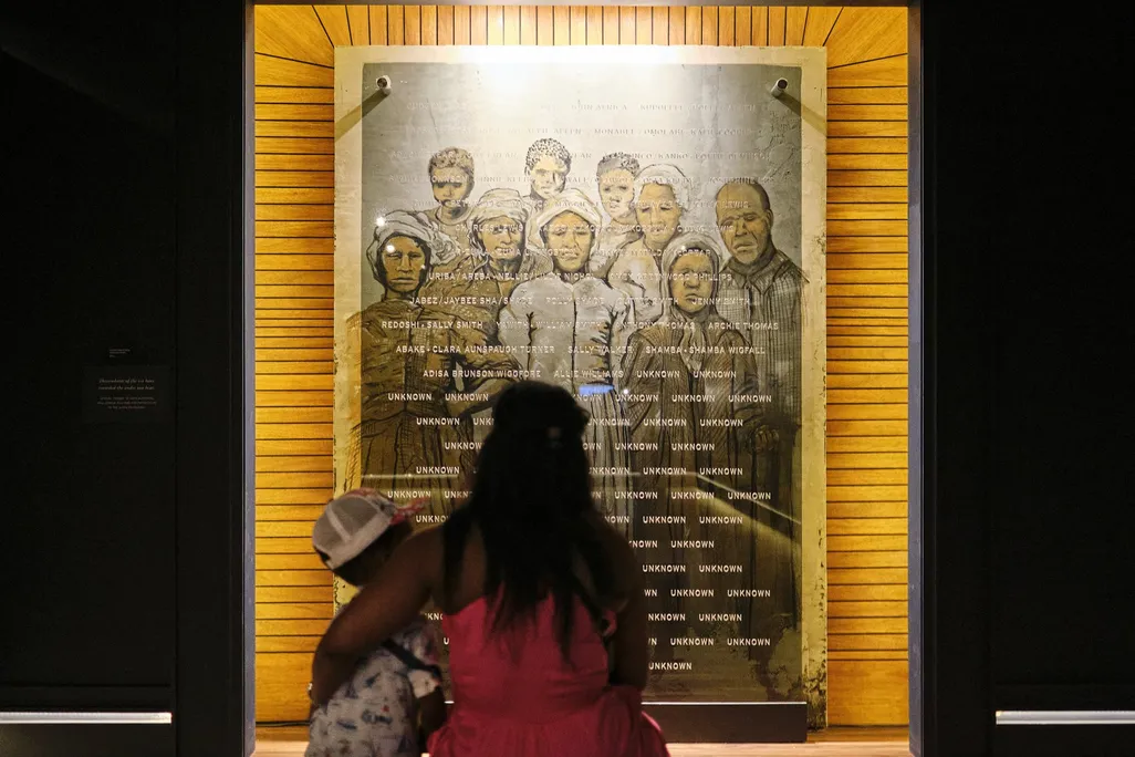 Woman holding child while looking at memorial wall inside museum