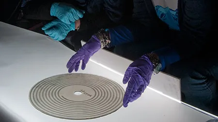 Curator Carlene Stephens, on left, and collections manager Shari Stout look at a glass disc containing a sound recording from the 1880s.