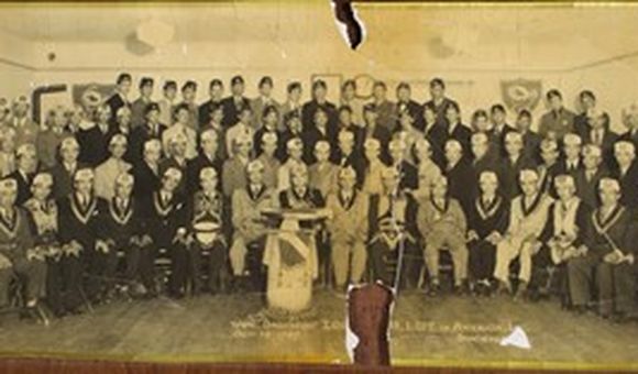 50 plus men in corresponding lodge regalia are posed in four staggering rows in a gathering hall.