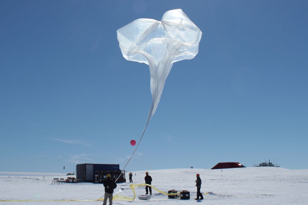 scientists inflate a large white balloon on an icy landscape