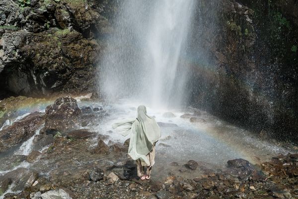 A Muslim woman standing under a waterfall. thumbnail