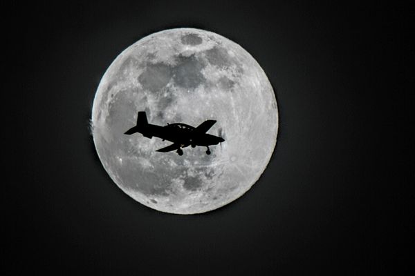 A plane flying past the full moon thumbnail