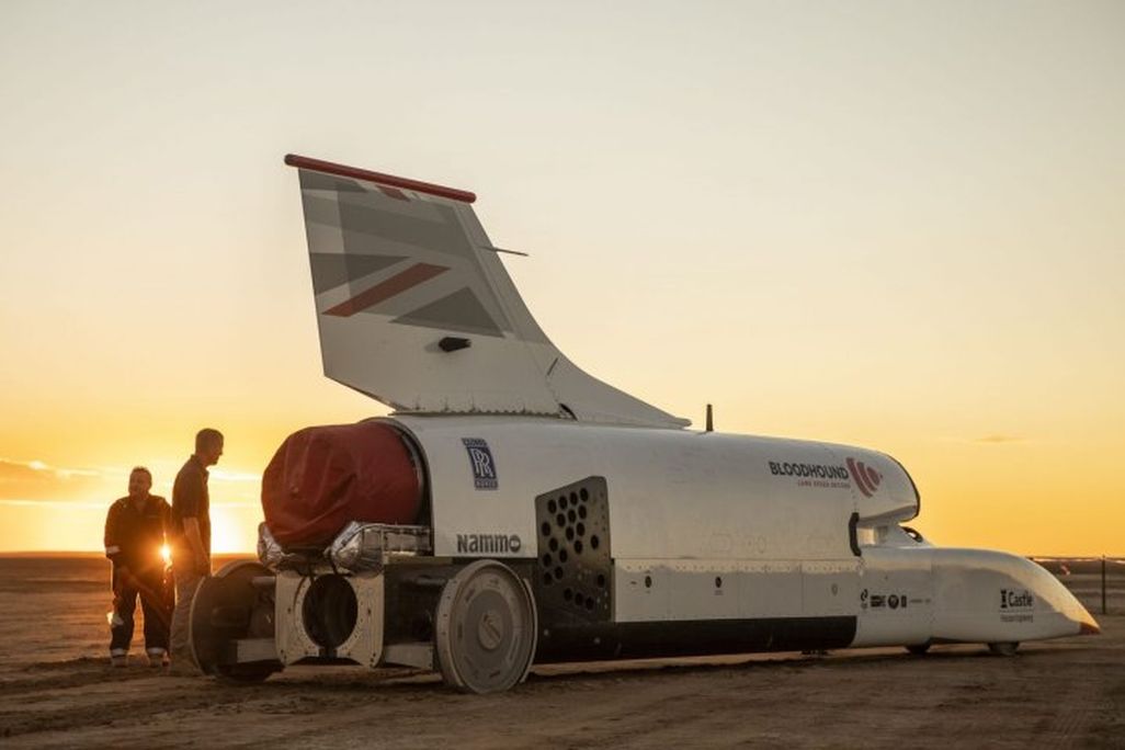An image of the supersonic car at sunset with two people standing to its left.
