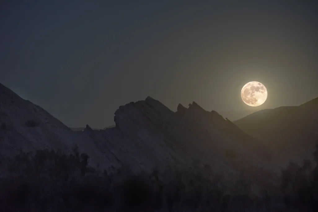 full moon glowing above rocky highlands in the foreground
