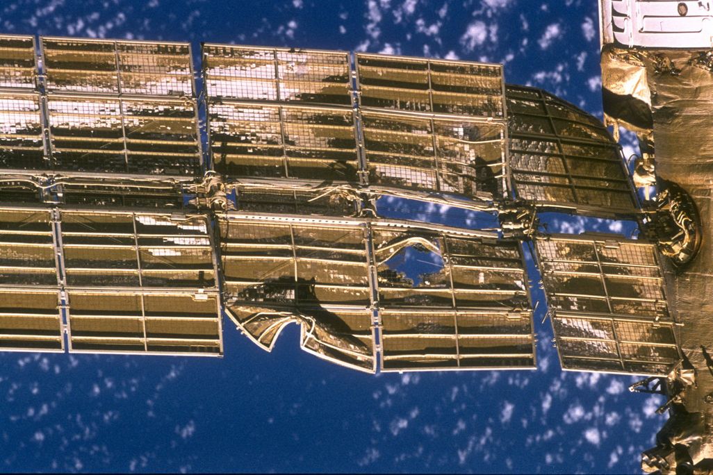 A golden solar panel on the Mir Space Station with a hole and a few tears from a collision