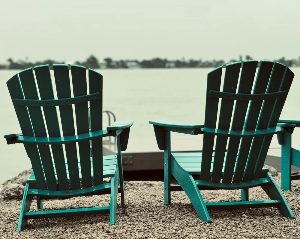 The green color of the beach chairs stands out against the grey misty sky and canal.