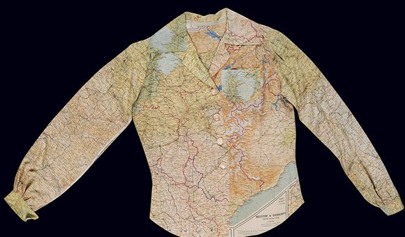 A ladies long-sleeve blouse fastened by four plastic white buttons hangs against a dark background. The blouse features a multi-color map pattern printed on a white silk background.