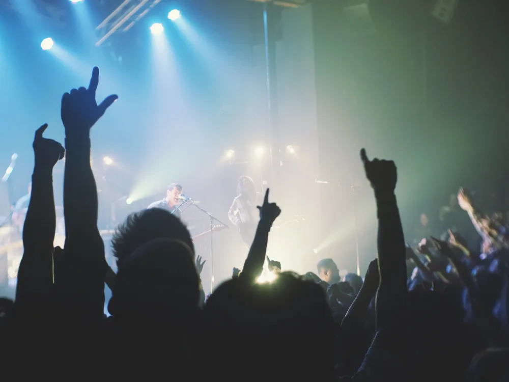 A stock photograph of a concert, with silhouetted fans raising their arms in the foreground and a singer on stage in the background.