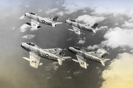 Four vintage fighter jets flying in a tight "finger-four" formation above a thick layer of white clouds in a black and white photograph.