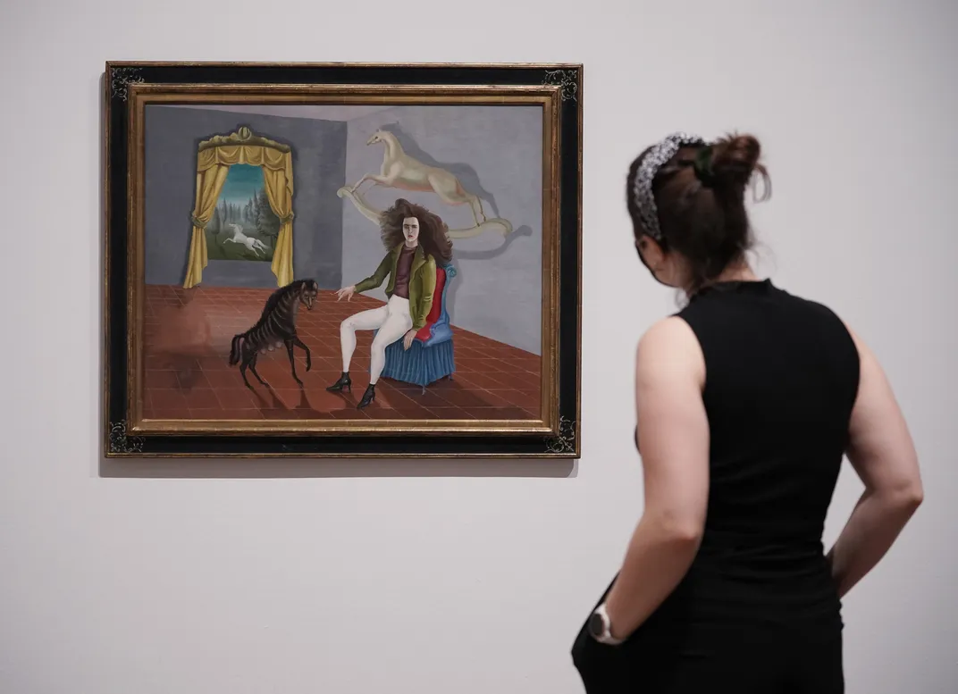 A gallery staff member stands next to a painting by Leonora Carrington, Self Portrait, 1937-38