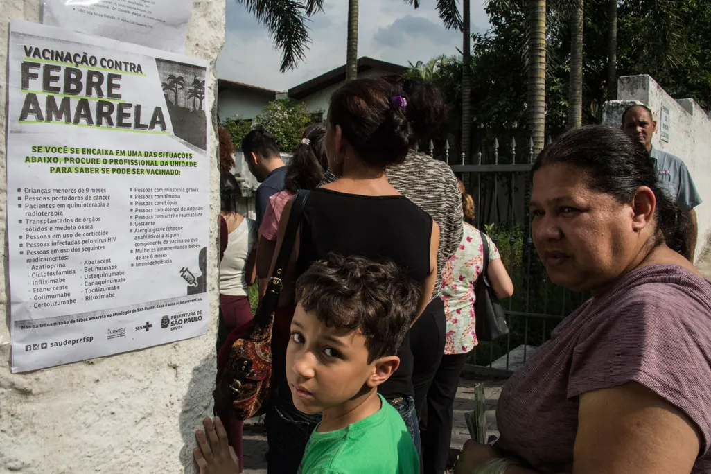 A young boy and a woman standing next to a sign that says yellow fever in Portuguese