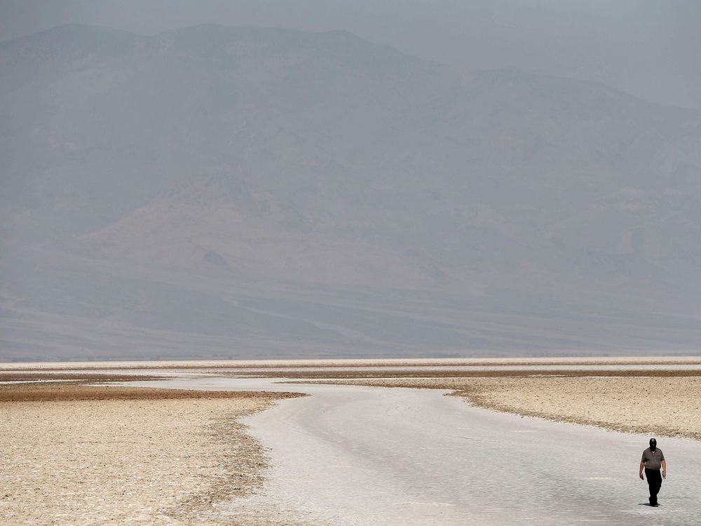 A large expanse of flat, sandy ground, with the faint outline of a hill rising in the distance; one lone traveler is walking in the lower righthand corner of the frame, looking very small compared to the landscape