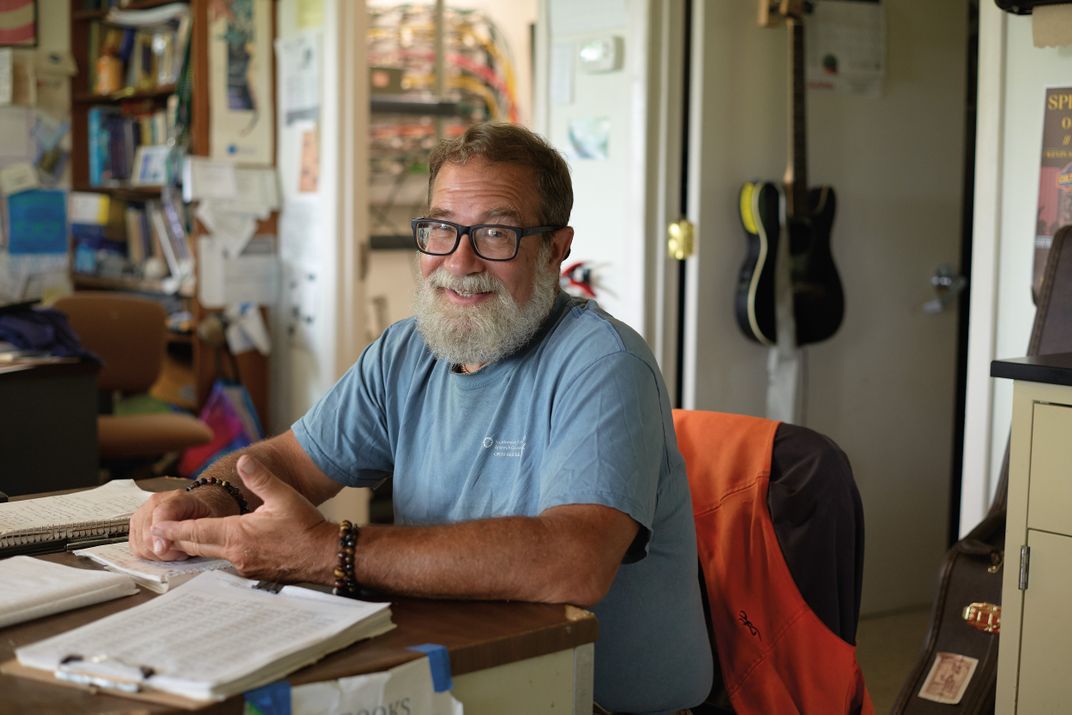 a bearded man with glasses sits at his desk