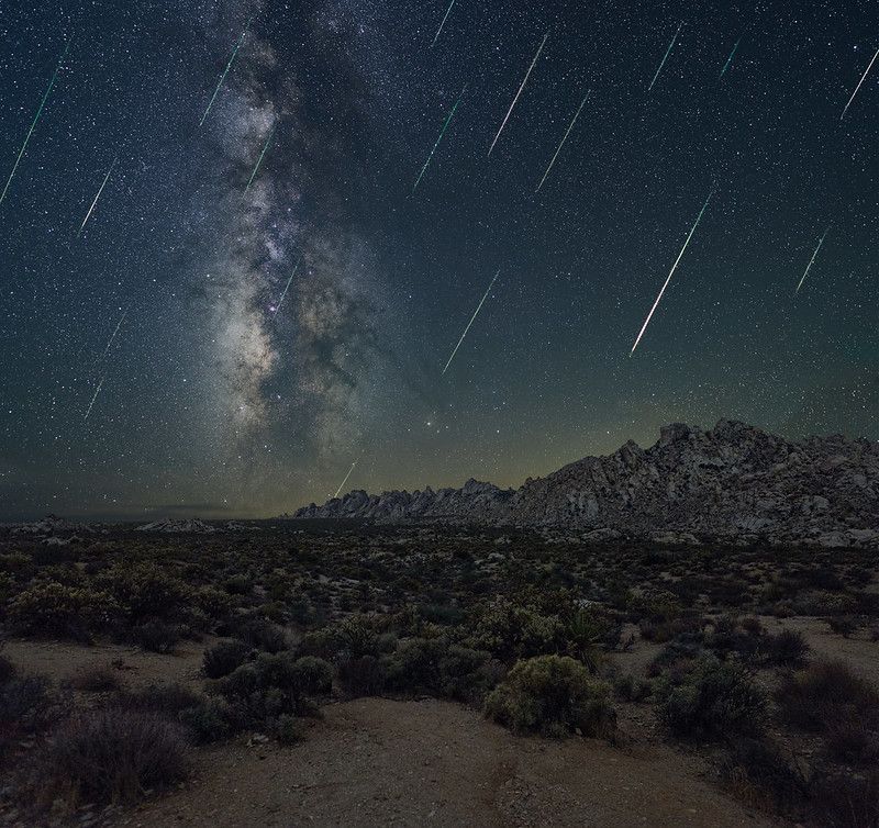 several meteors fall diagonally down in front of a sky view with the Milky Way