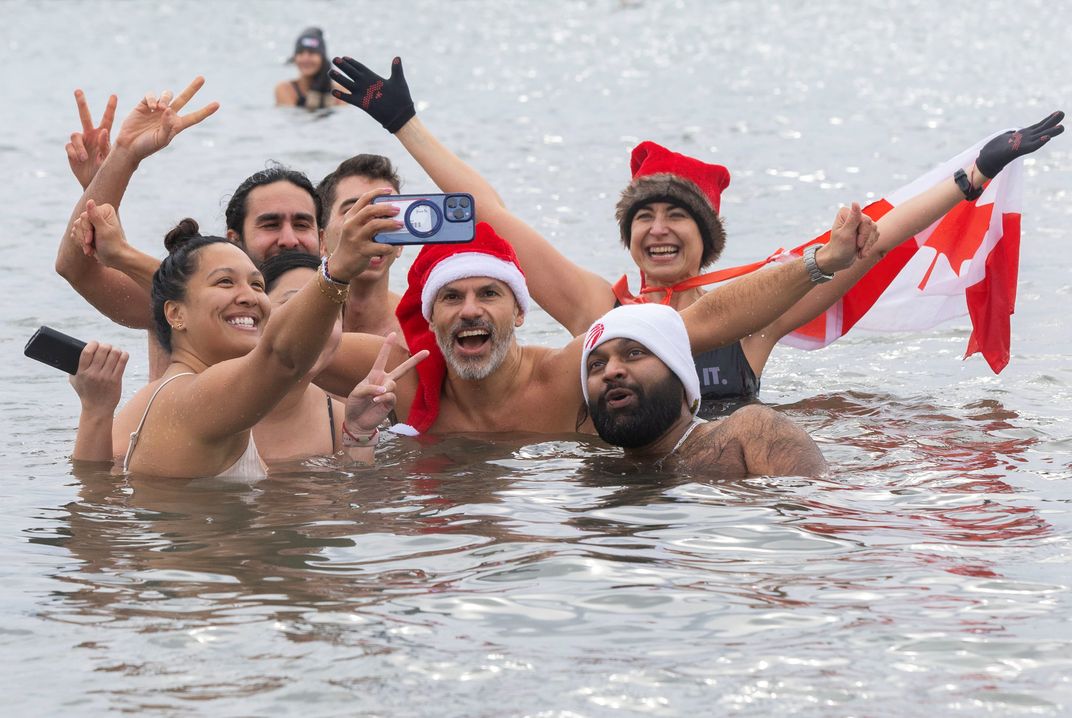 people take a selfie in the water, one wearing a santa hat and one with a Canada flag
