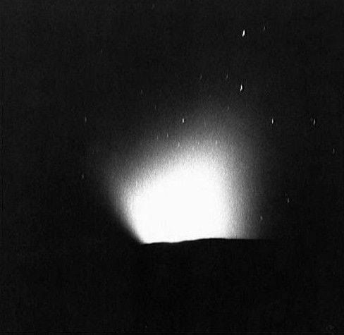 a white glowing blob in a black-and-white image emerging from a dark horizon