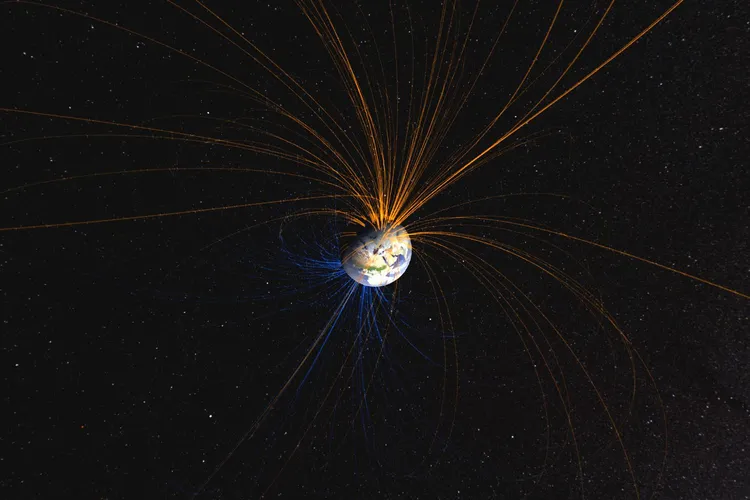 Earth&rsquo;s magnetic field surrounds the planet, with illustrated field lines emerging from the north, in orange, and looping around to the south, in blue.
