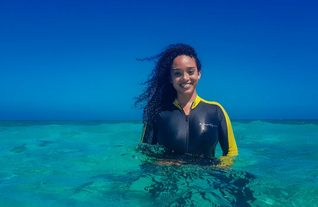 A woman in a wetsuit with curly hair smiles while swimming.