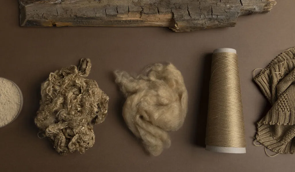 An overhead view of a piece of wood next to some yarn and knitted fabric