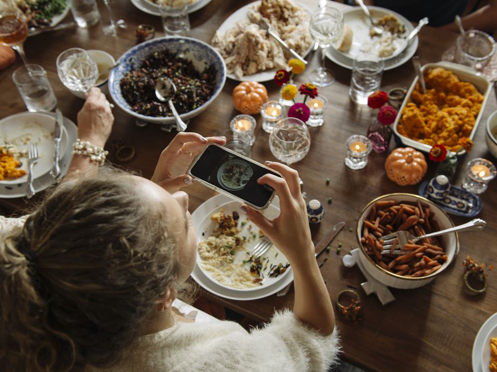 A teenage girl sitting at the dining table during Thanksgiving taking photos of the food with her smart phone