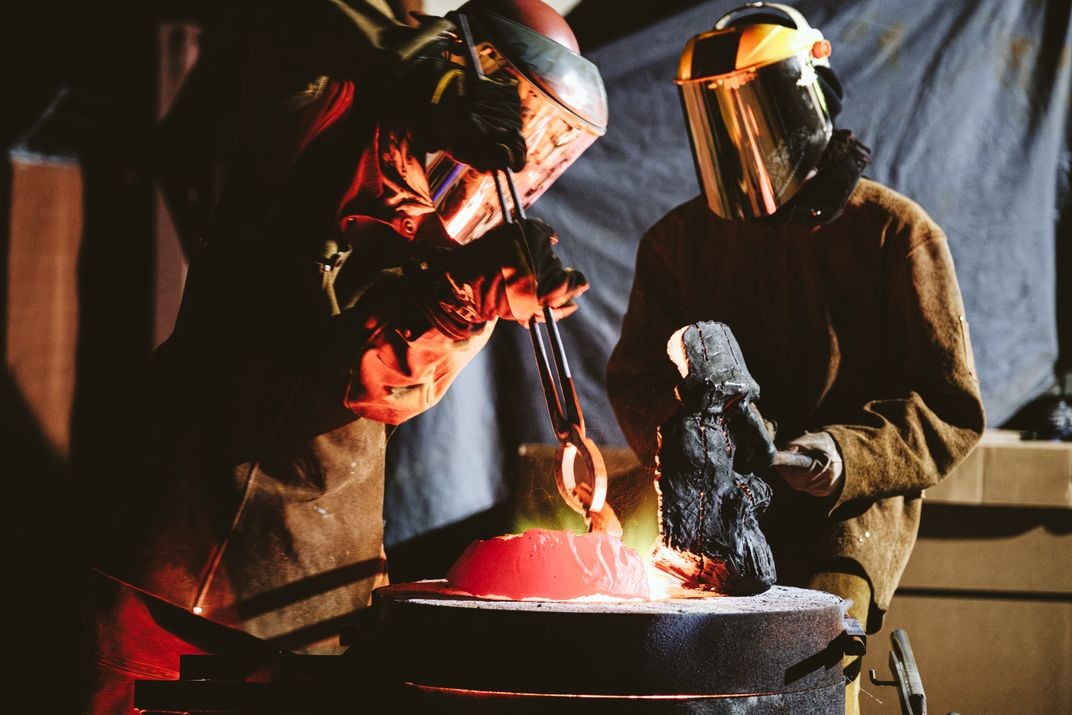 Foundry workers melting pieces of statue in furnace