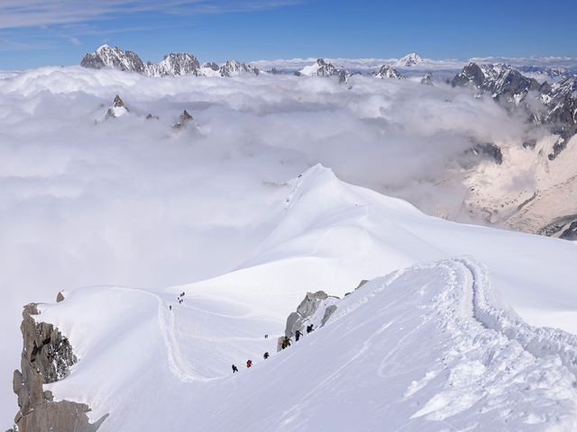 Alpinists ascend along a narrow ridge of ice and snow in the Mont Blanc massif.