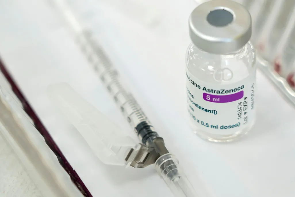 A vial of AstraZeneca vaccine sits on a white surface next to a capped syringe 