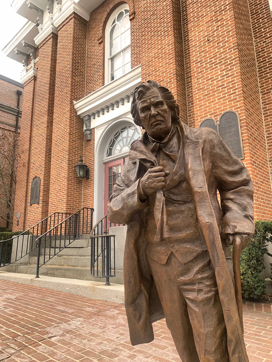 a statue of man with a cain in long overcoat stands in front of a courthouse