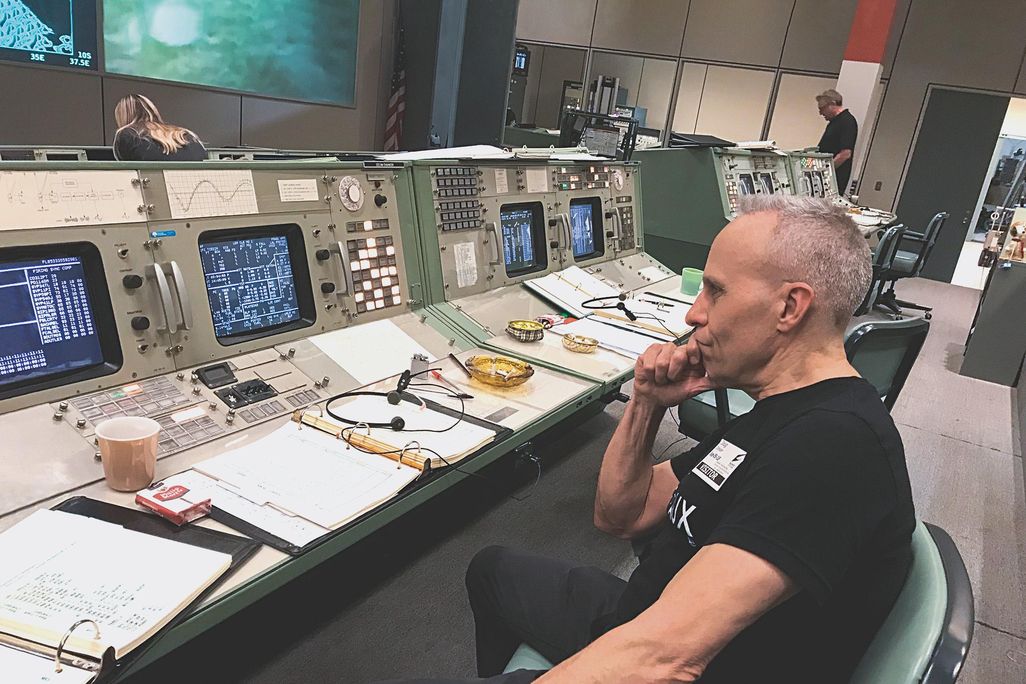 Doug Drexler seated in chair on mission control set