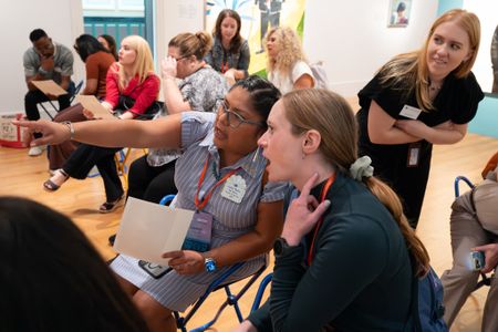 Two teachers sit side by side pointing out details in a museum gallery