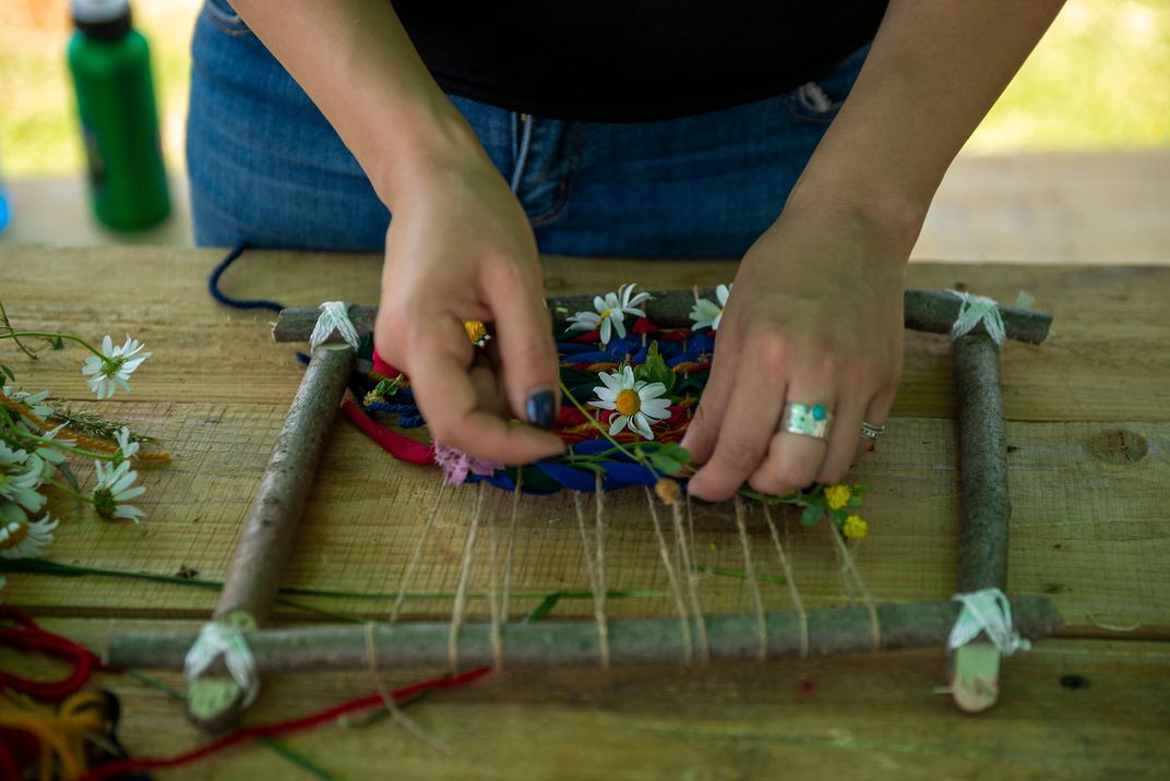 A person weaves on a handmade loom made from sticks tied together with twine.