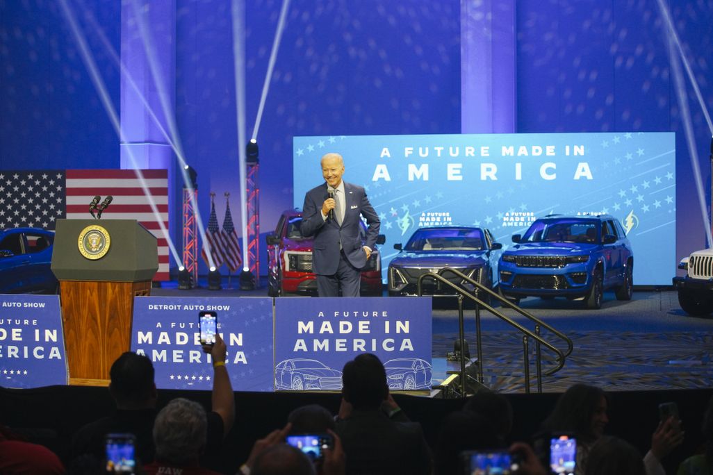 President Biden on a stage with cars and signs that read "A future made in America"