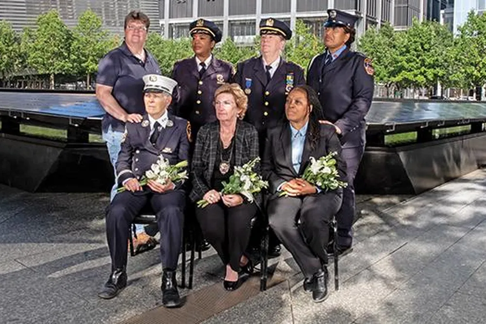 seven women first responders looking solemn, most in uniform, at the Ground Zero Memorial