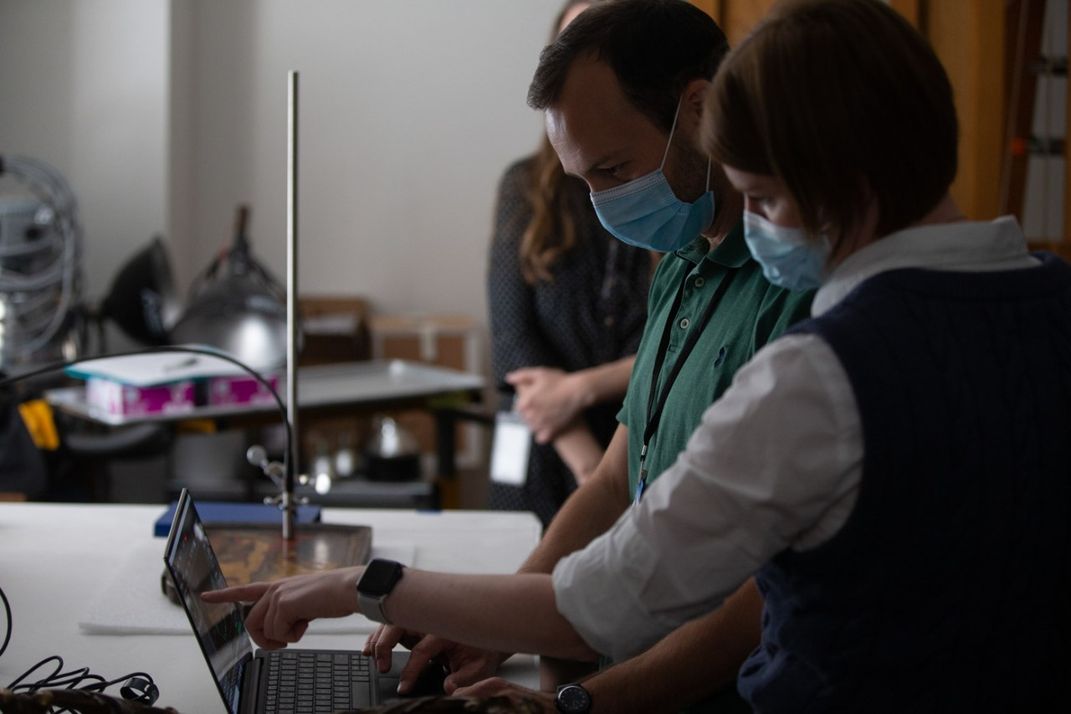 Pesquisadores em um laboratório apontando para uma tela de laptop