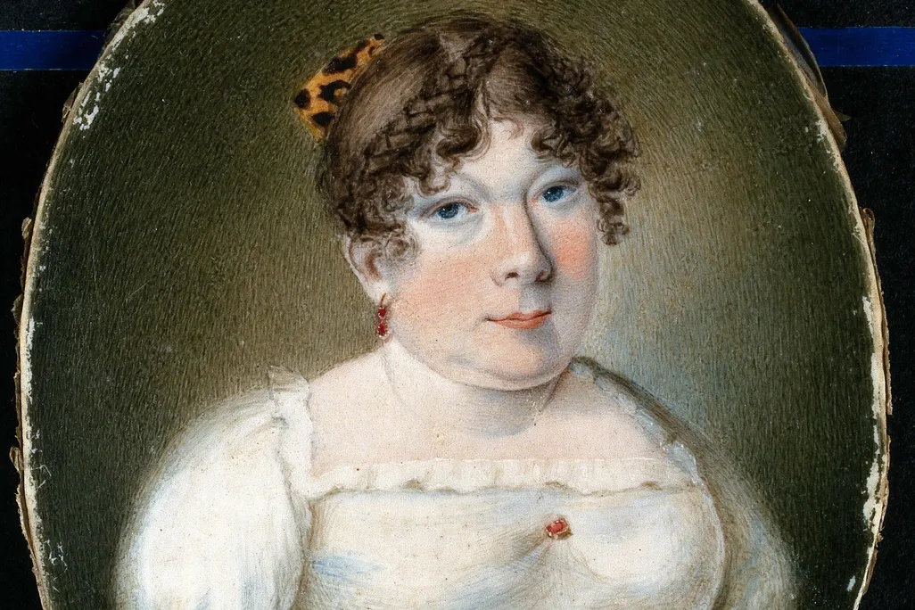 A miniature portrait of a white woman with curled brown hair in a white empress dress with a blue ribbon; her arms end below the shoulder, where her dress is pinned