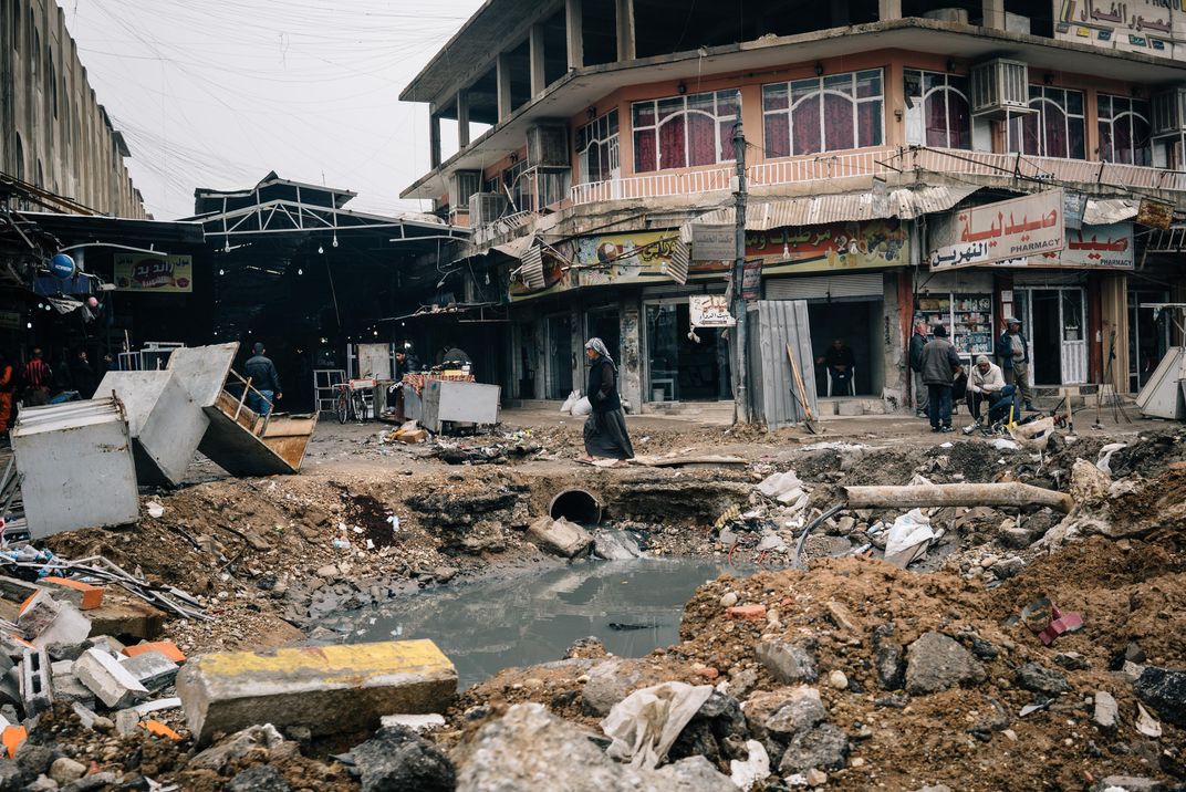 A man walks by a large crater, now filled with sewage, in war-ravaged east Mosul.