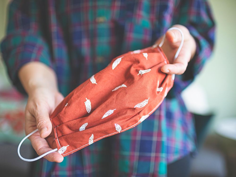 A person holds a sewn handmade fabric mask. 