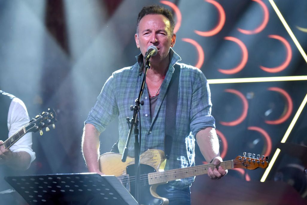 middle-aged man singing on stage into microphone and playing