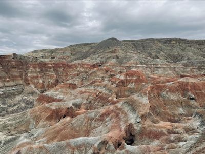 A grey, orange, and brown expanse of layered rock formations under a gray sky.