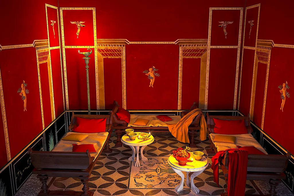 A red walled room with white and black tiled mosaic, with a large decorative piece in the center of the floor that depicts a grape vine extending from a vase and three low beds against each wall