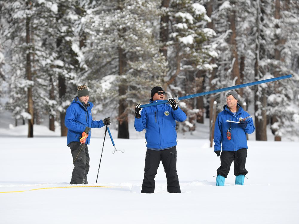 Three men in blue coats standing in the snow with equipment