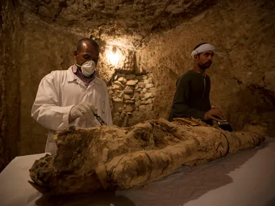 Egyptian excavation workers work on a mummy in a newly discovered tomb in Luxor, Egypt