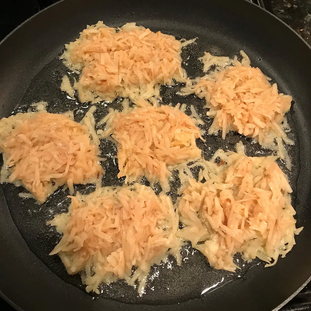 Undercooked potato pancakes in a pan, frying.