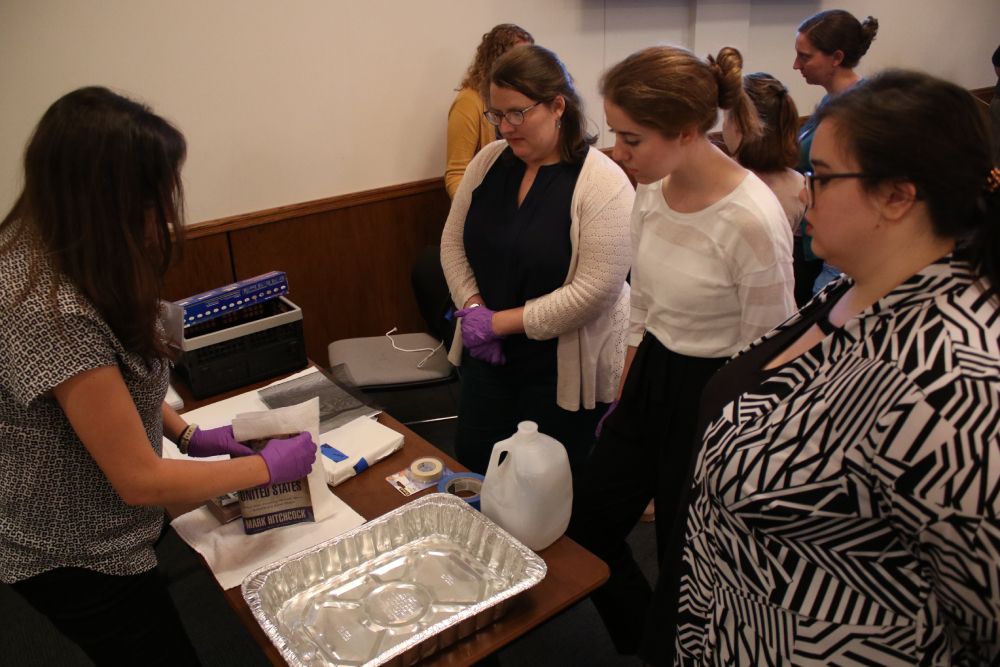 Visitors at an exhibit table watching a demonstration.