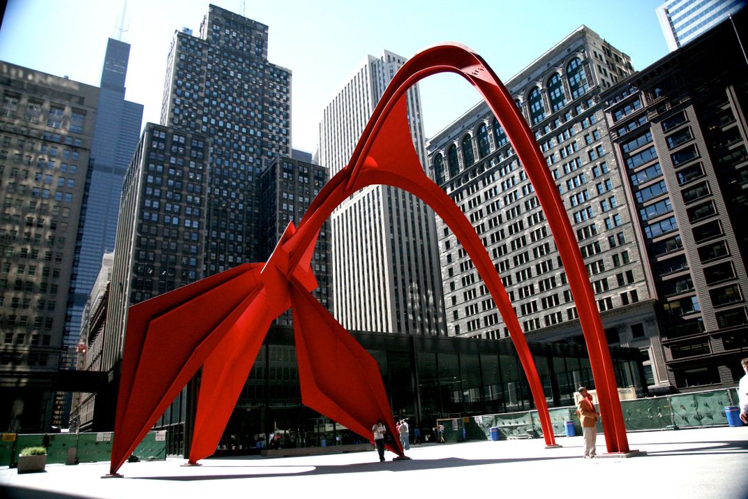 A bright red sculpture, huge, towers over a plaza; it's composed of two long looping arches and three shorter ones clustered at the base