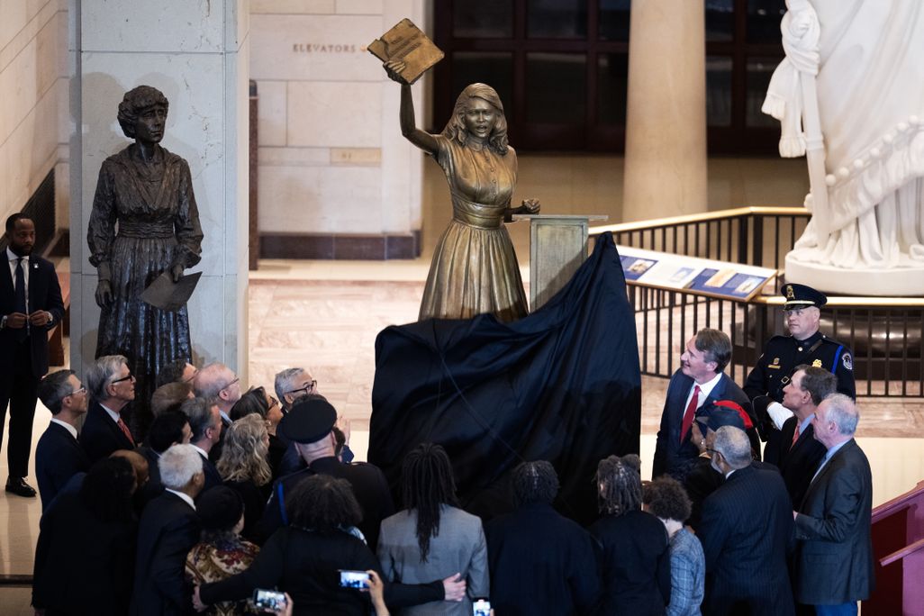 People gathering around a bronze statue of a woman holding up a book
