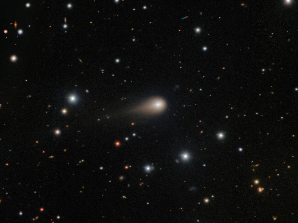 a deep field view of the sky, with a glowing comet with a small tail in the middle