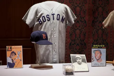 Hat and jersey worn by Ted Williams during his Red Sox reign. The autographed portraits, from left to right, are of Williams, Babe Ruth, and Hank Aaron. Foregrounded is a baseball signed by the members of the "Murderers' Row" 1927 Yankees.